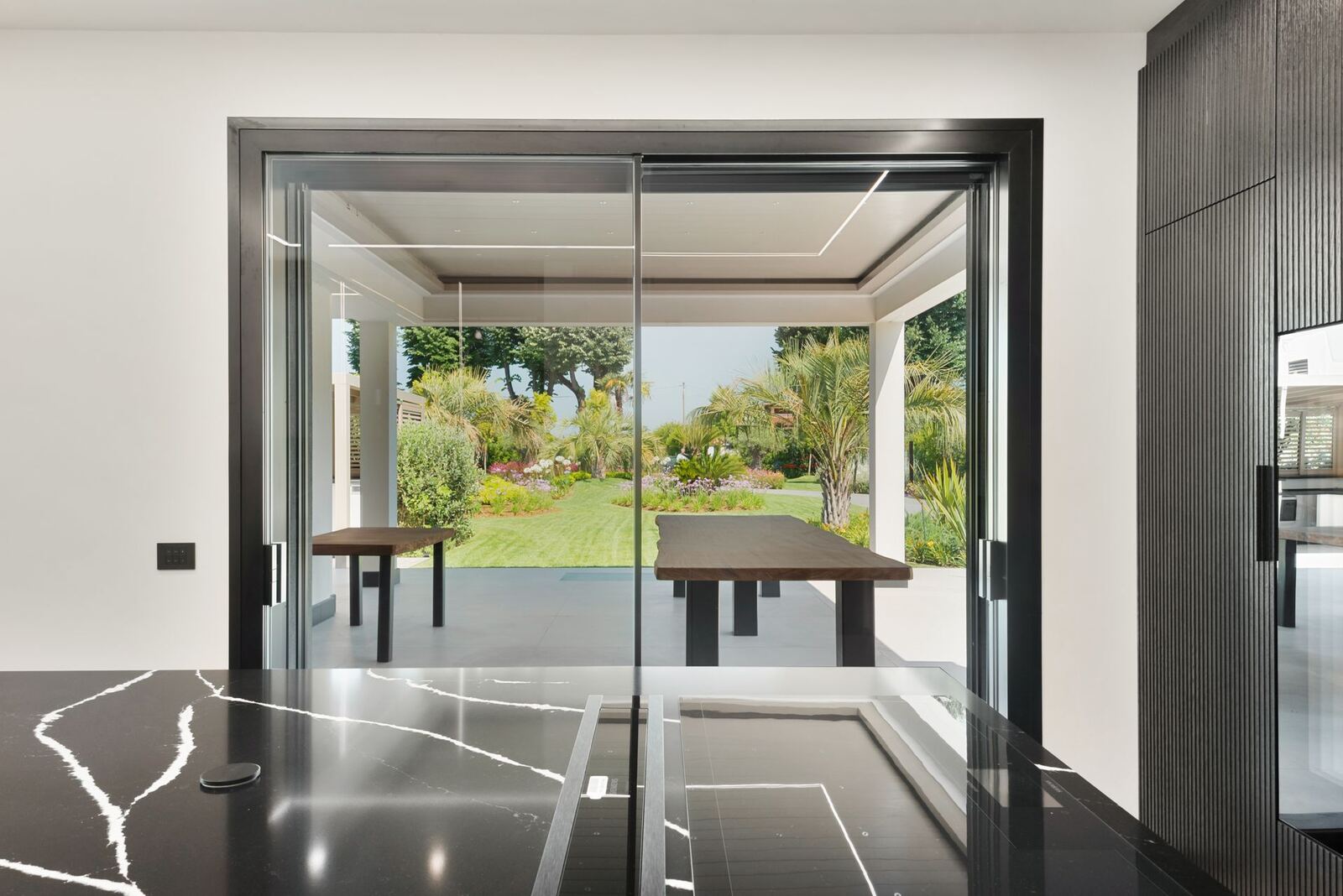 Sala da pranzo con vetrata scorrevole e piano in granito nero, vista sul giardino